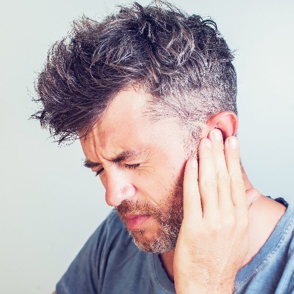 A man suffering hold his ears in pain suffering from tinnitus (ringing in the ears) 